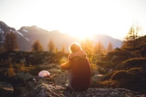 A woman sits on a rock enjoying the serene mountain view at sunrise in Sachseln, Switzerland.